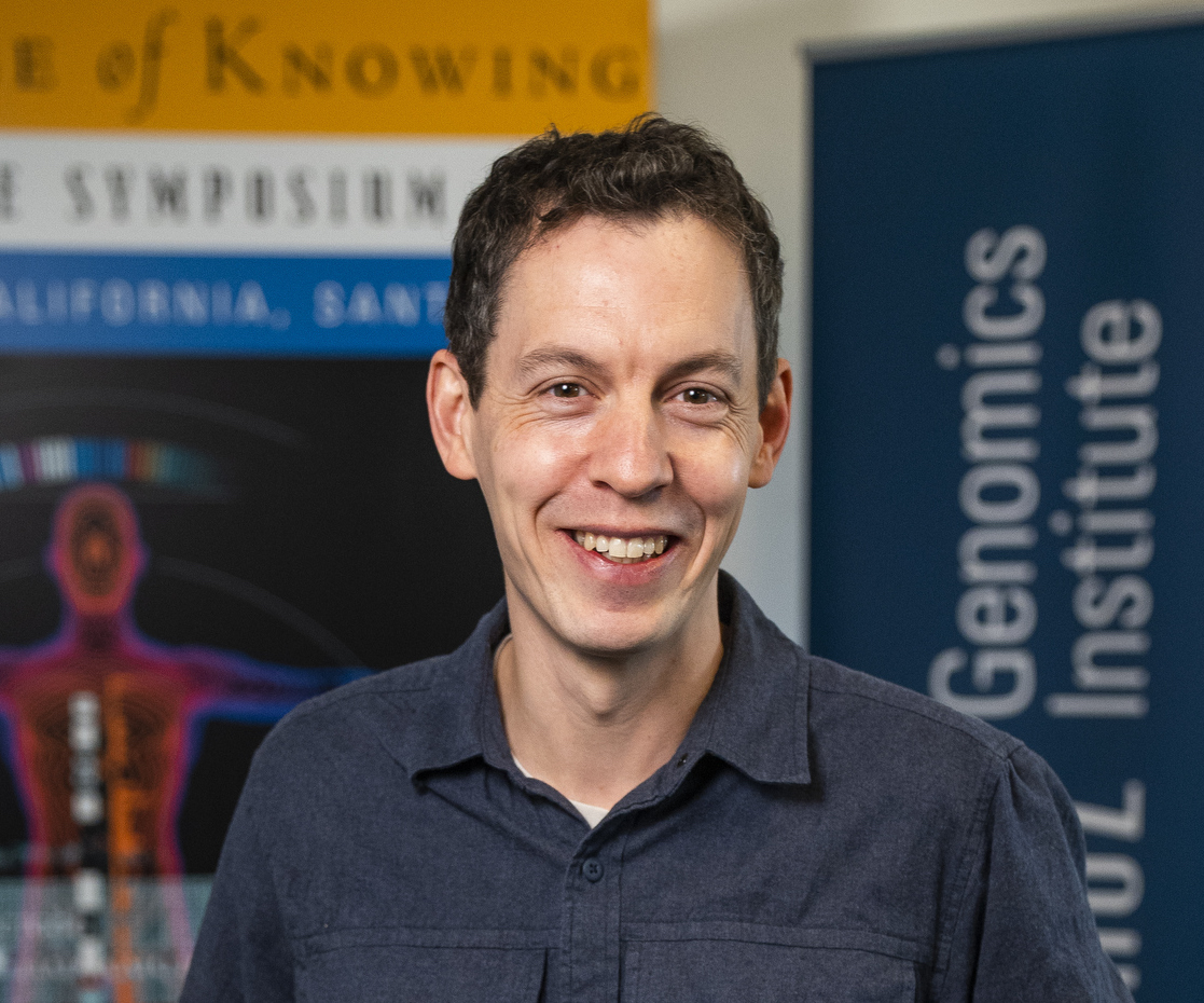 A photo of Benedict Paten in front of a banner for the Genomics Institute at UCSC. 